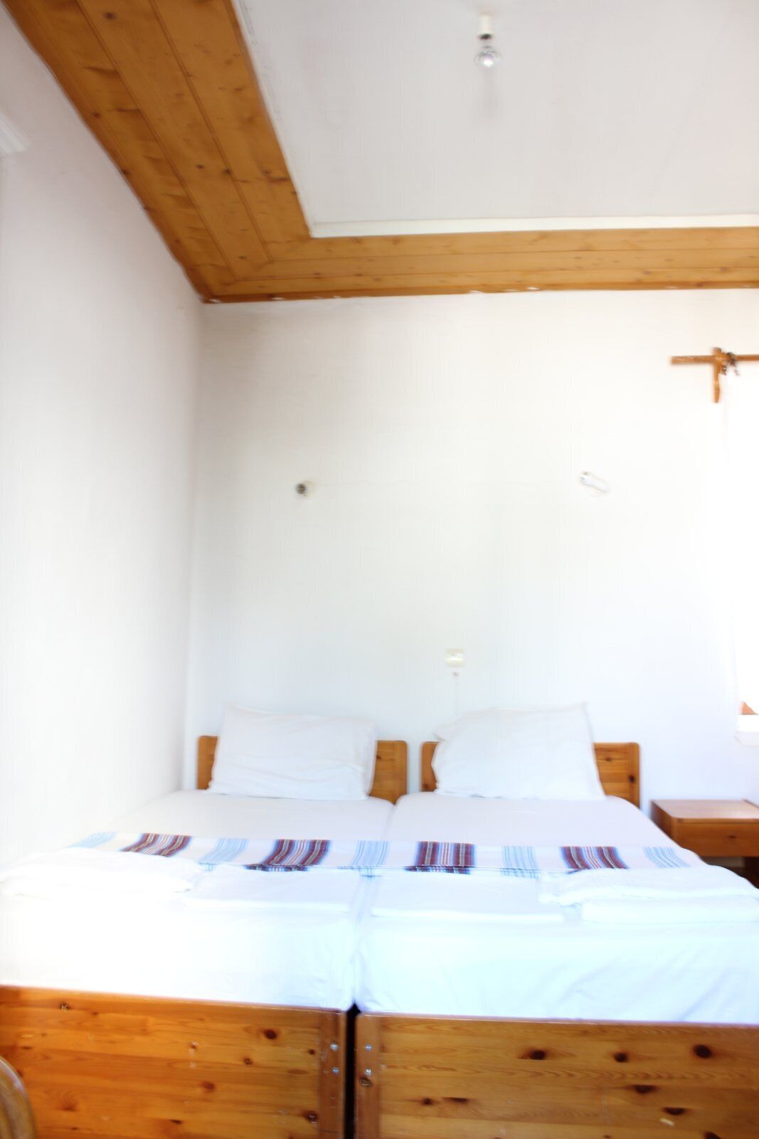 A room with a wooden bed frame, white bedding, and a wooden ceiling.