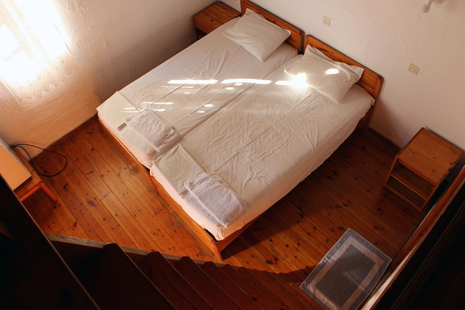 Una cama individual con ropa blanca de cama y almohadas, cabecera de madera y una mesita de noche de madera.