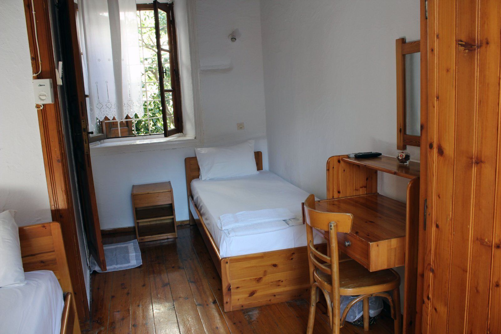 A small, wooden room with a bed, a wooden desk, a chair, and a window with curtains.