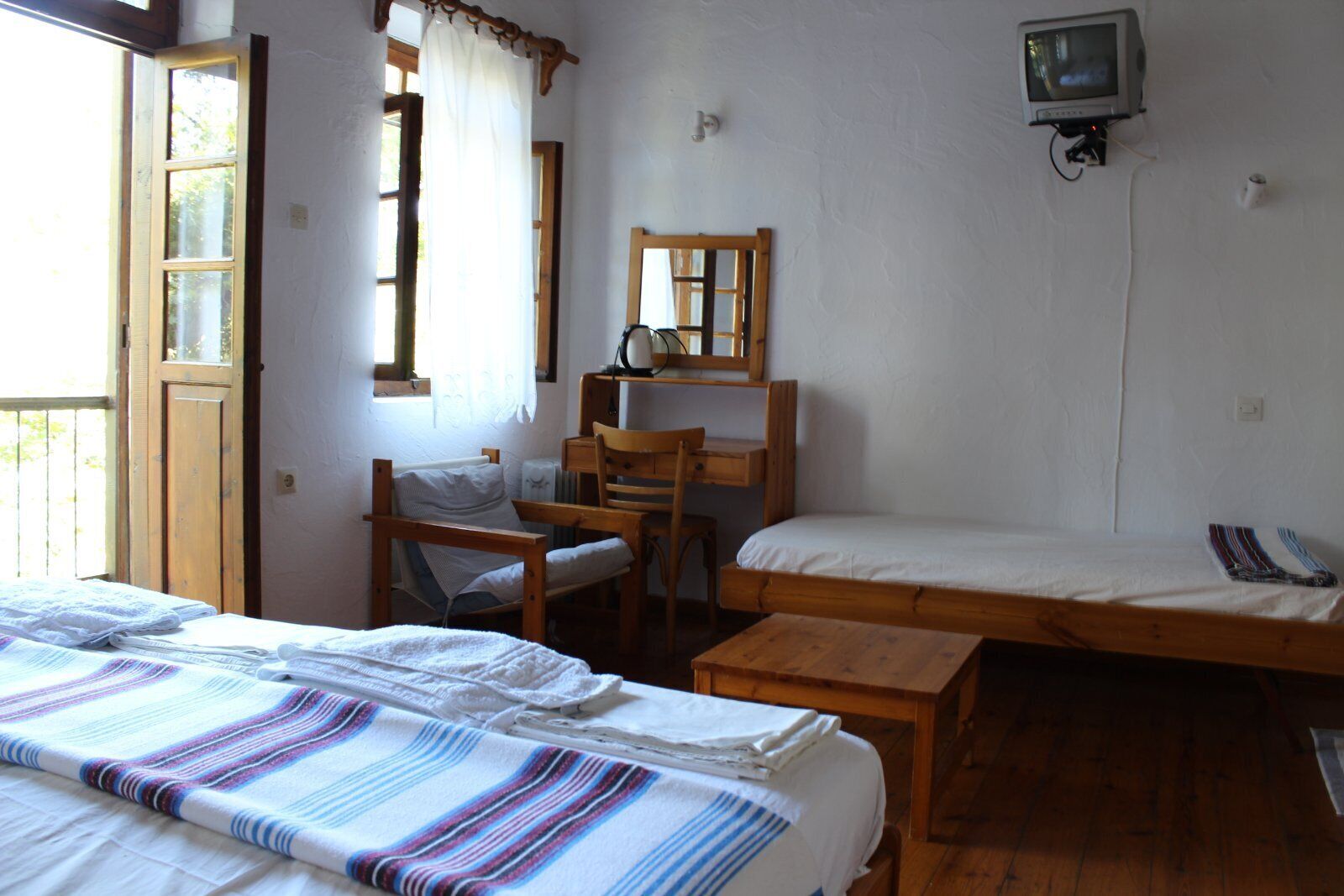 A room with two beds, a desk, a chair, a television, and a window with curtains.