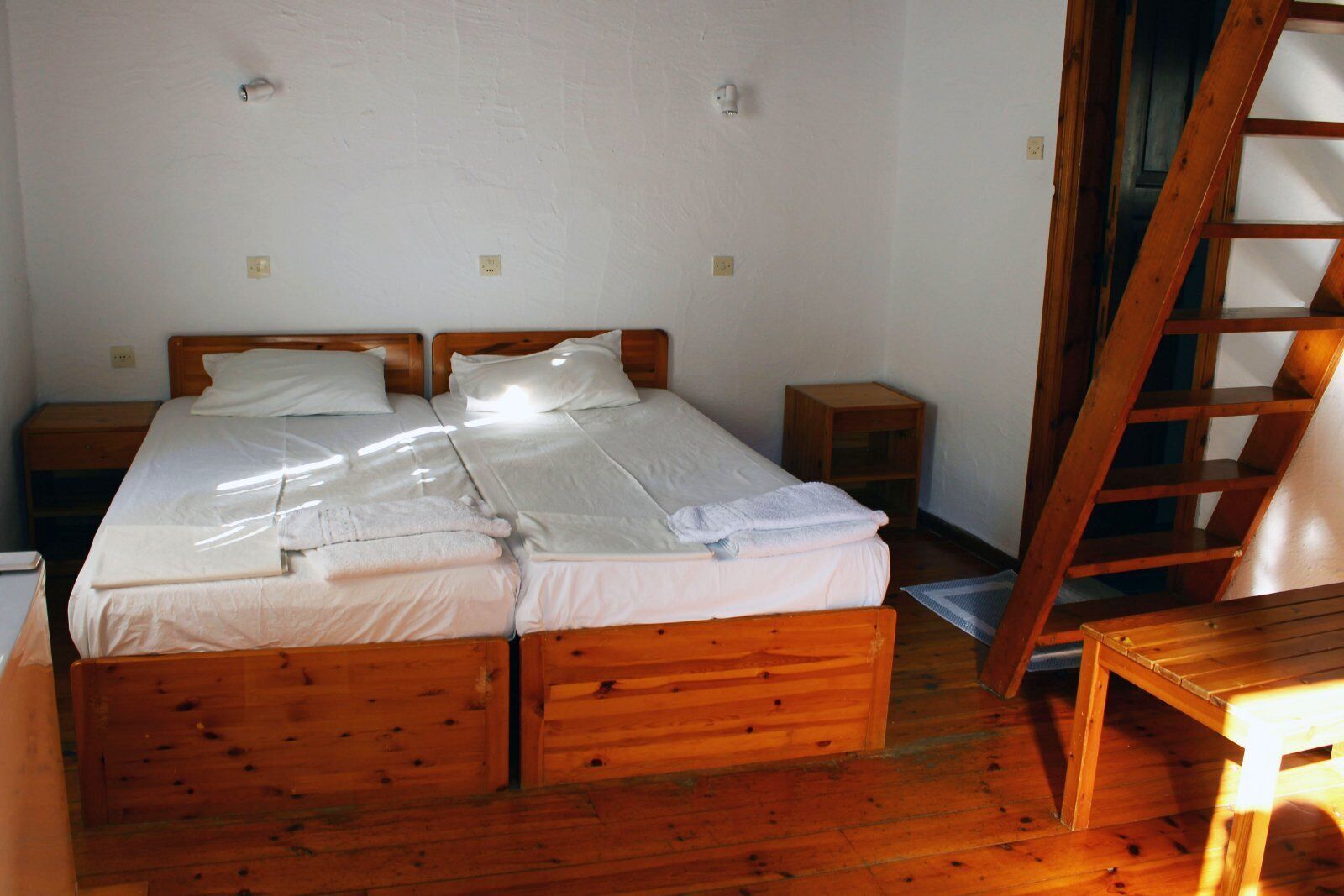 Quarto com duas camas de madeira, uma escada de madeira e uma pequena mesa de madeira.