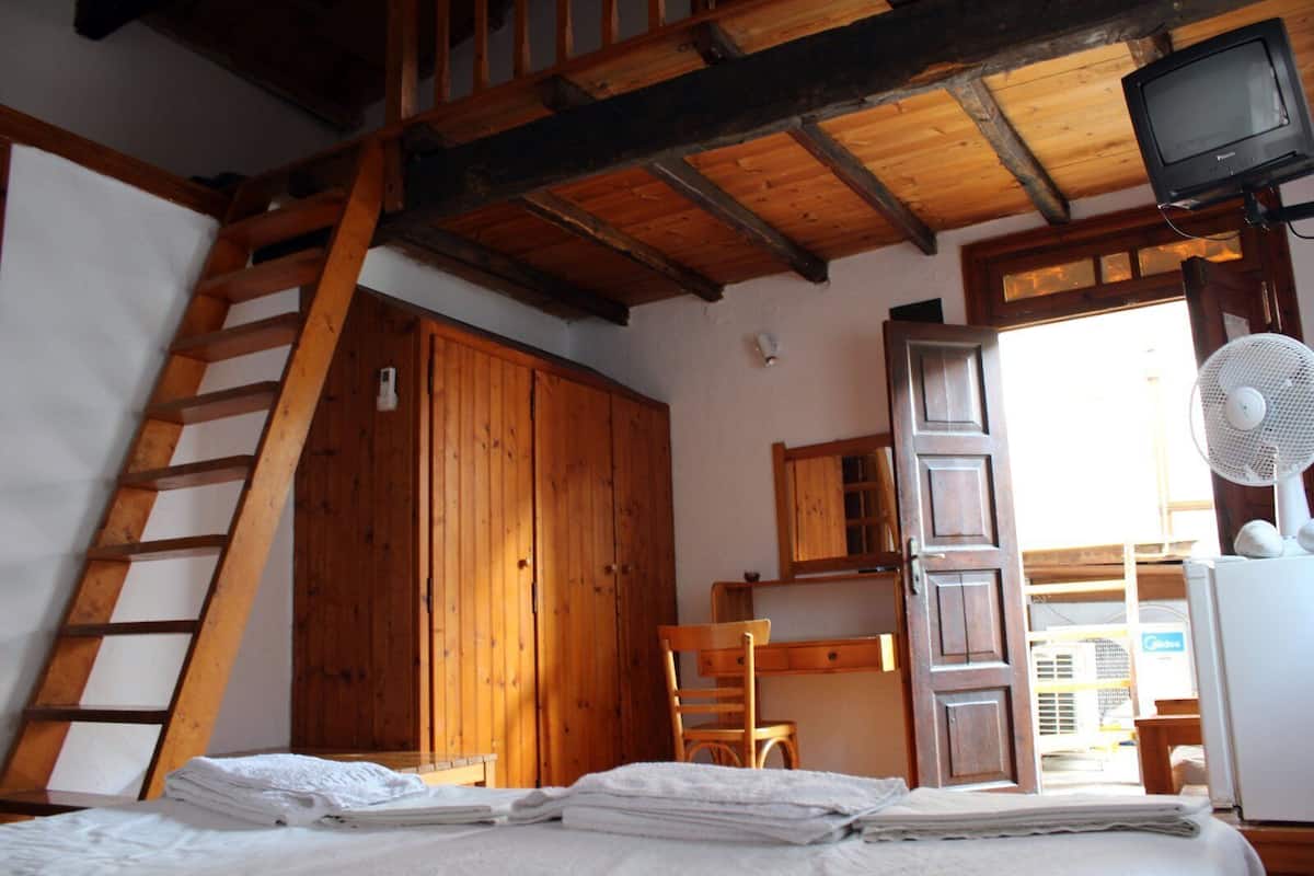 A wooden room with a bed, a chair, a desk, a ladder, and a television.
