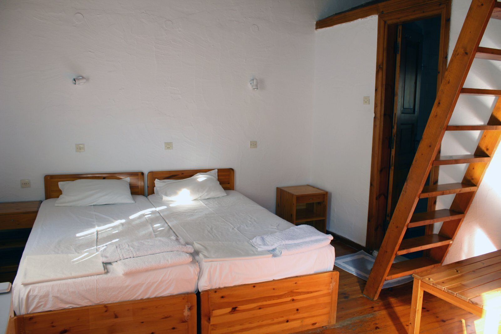 A bedroom with two wooden beds, a wooden ladder, and a small wooden nightstand.
