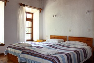Quarto com cama, cabeceira de madeira, janela com cortinas e piso de madeira.