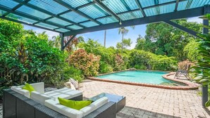 A covered outdoor area with a swimming pool, surrounded by lush greenery and furnished with outdoor seating. - Comino on Connemara - Lagoon Style Pool (Trinity Beach)