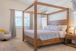 A four-poster bed with a wooden frame, a bedside table with a lamp, and a chair with a yellow cushion. - Comfy House, Private Backyard w/ Pool, BBQ, Citrus (Surprise)