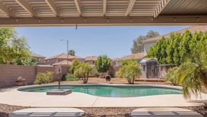 Un jardin avec une piscine, un patio couvert et une maison avec un toit en tuiles.