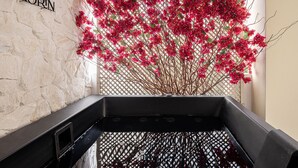 Un área de spa con pared de piedra, una bañera negra y una planta con flores rojas.