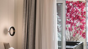 Un dormitorio moderno con cama, cortinas, una lámpara circular y vistas a flores rosadas a través de una ventana.