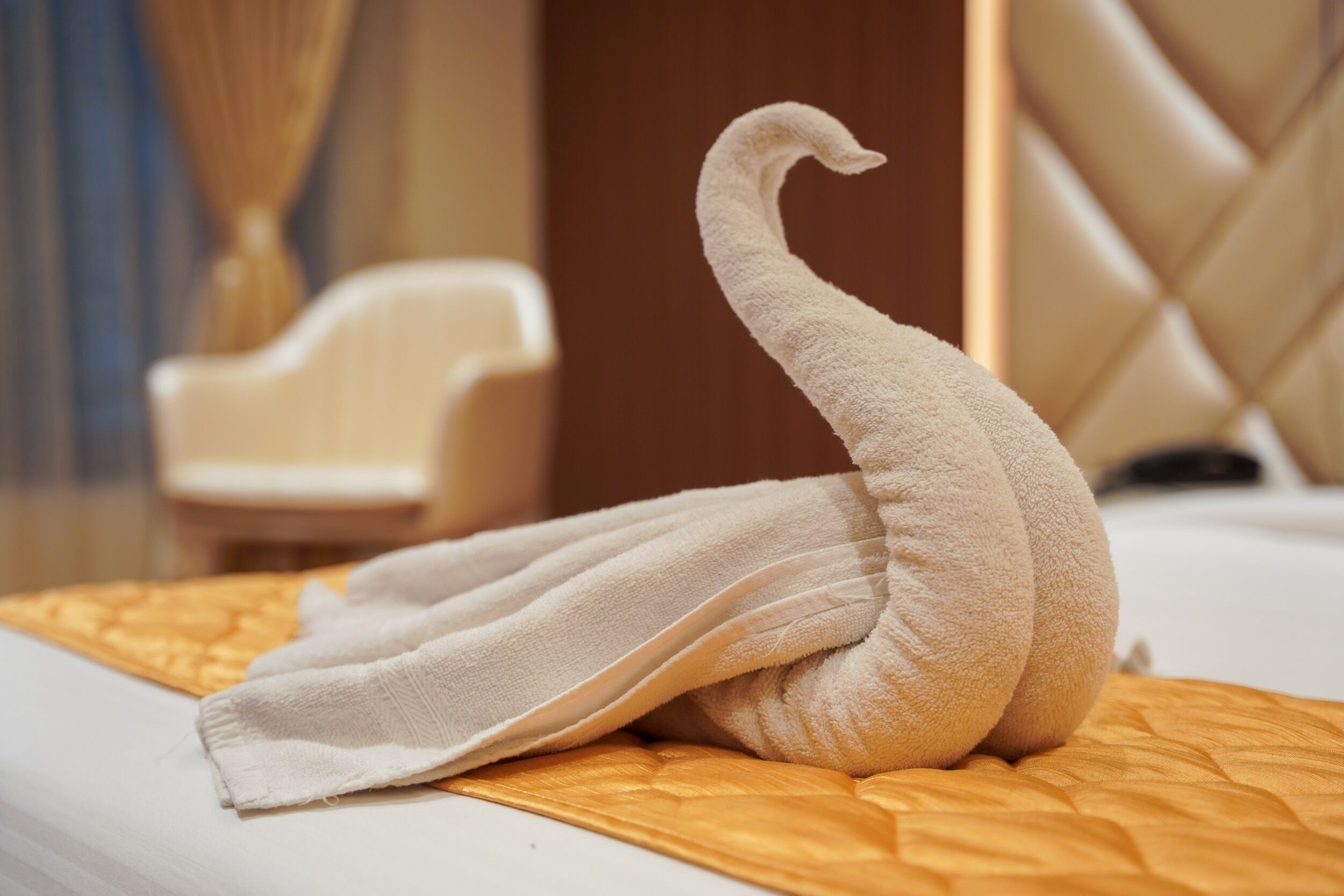 A swan-shaped towel on a bed with a quilted orange cover.