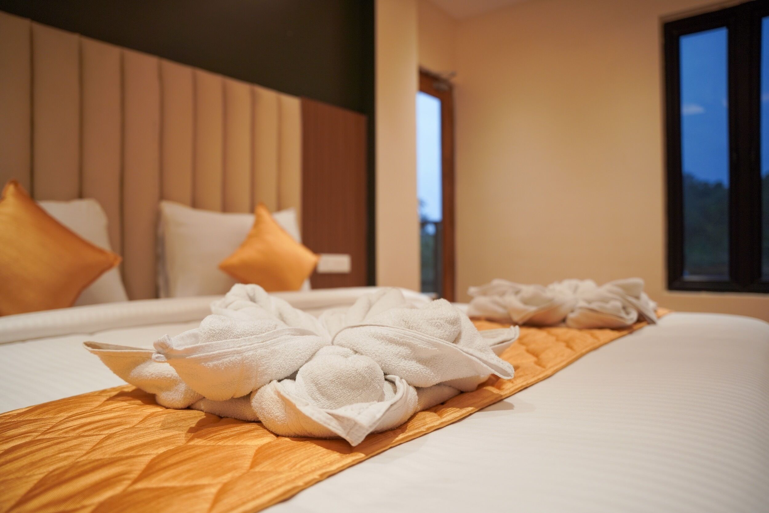 Una cama bien hecha con toallas y una bandeja de madera, cabecera de madera y ventana con vistas.