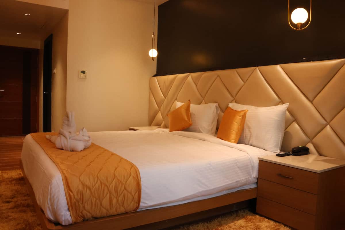 A hotel room with a large bed, a headboard with a diamond pattern, and a bedside table with a lamp.