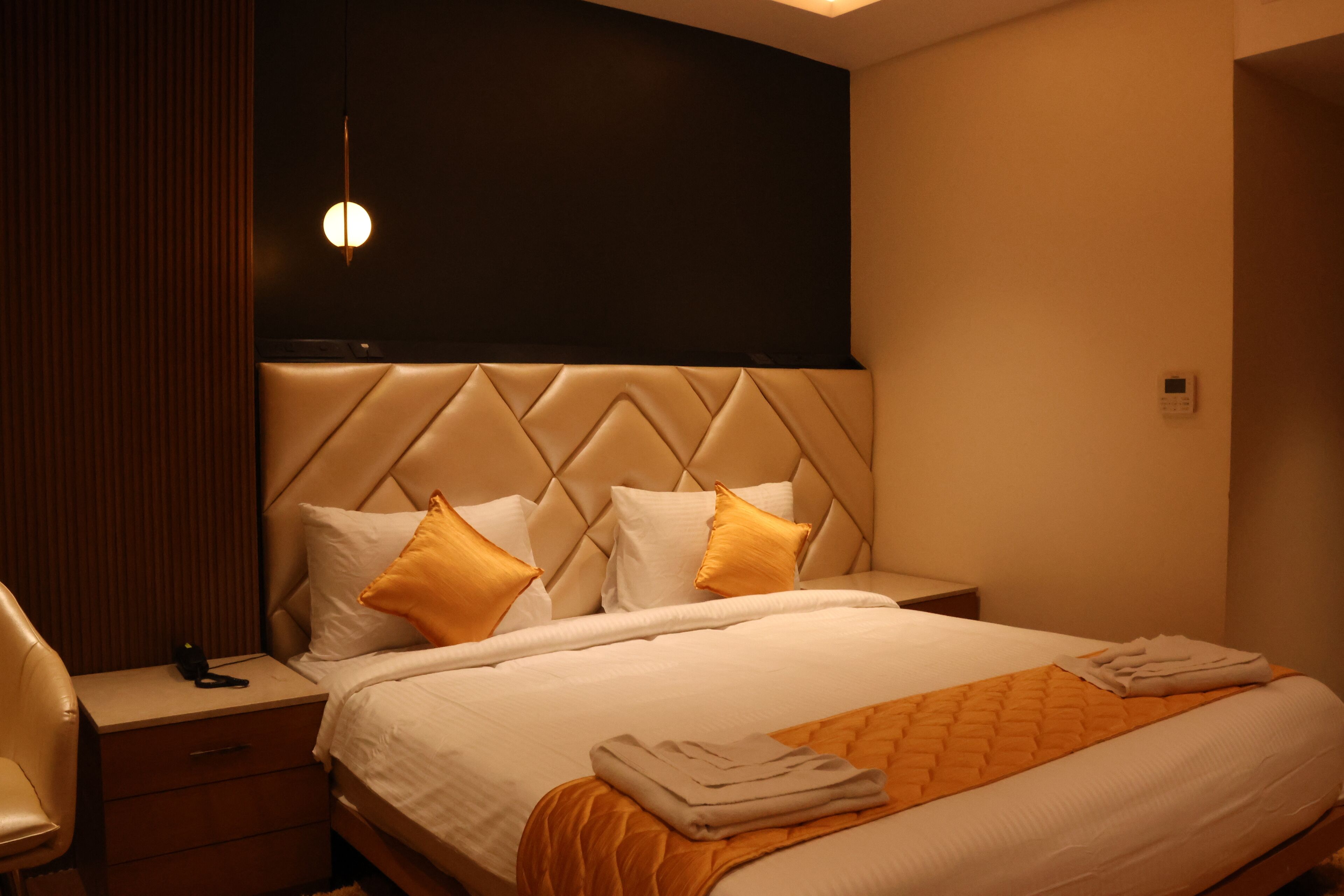 A hotel room with a large bed, a headboard with a diamond pattern, and a bedside table with a lamp.