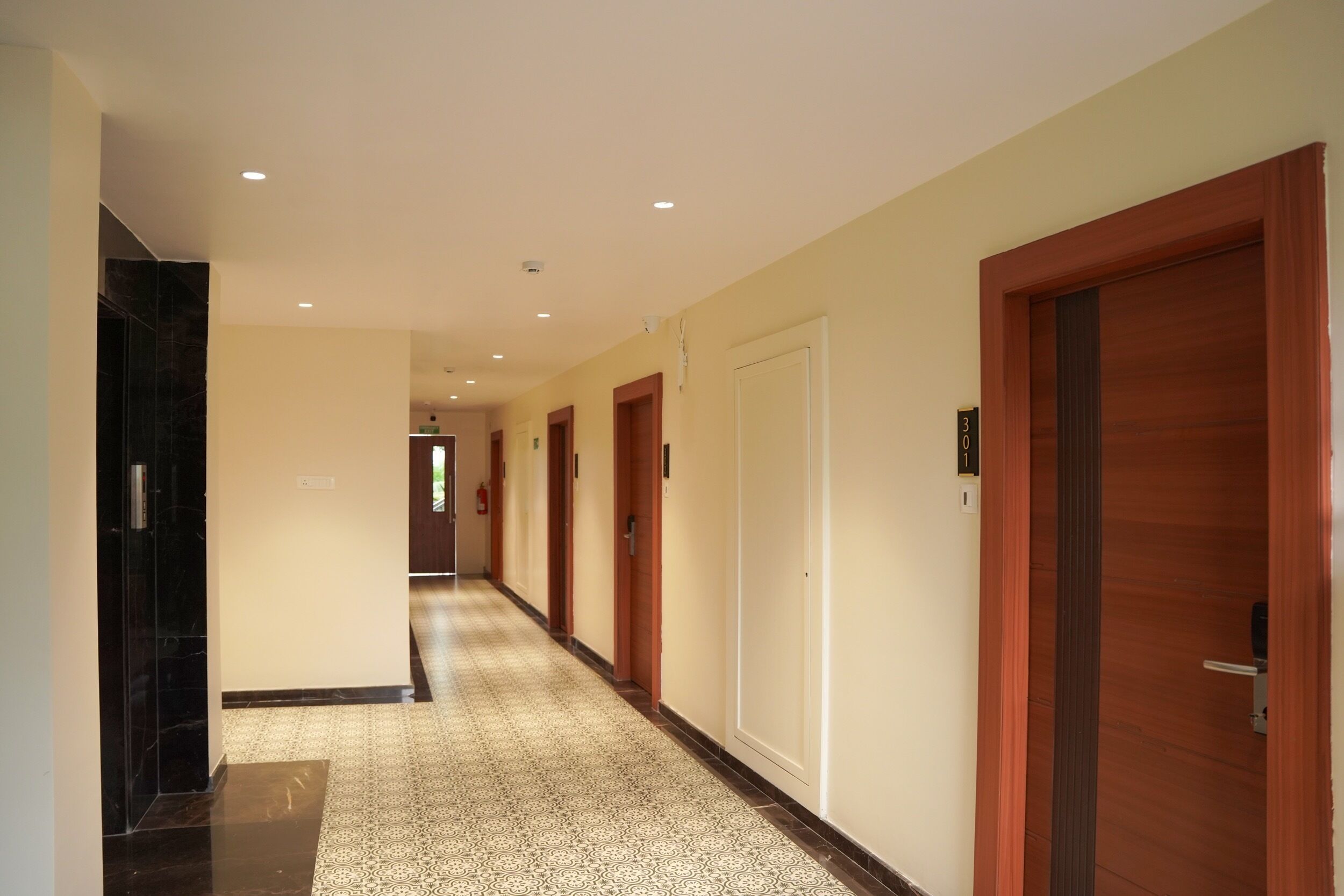 A hotel hallway with multiple doors, a patterned carpet, and a tiled floor.