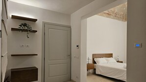 A bedroom with a bed, bedside tables, a wall-mounted shelf with a plant, and a door.