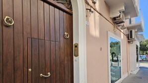 A wooden double door with brass handles, a glass door with a keypad, and a building facade with a number sign.