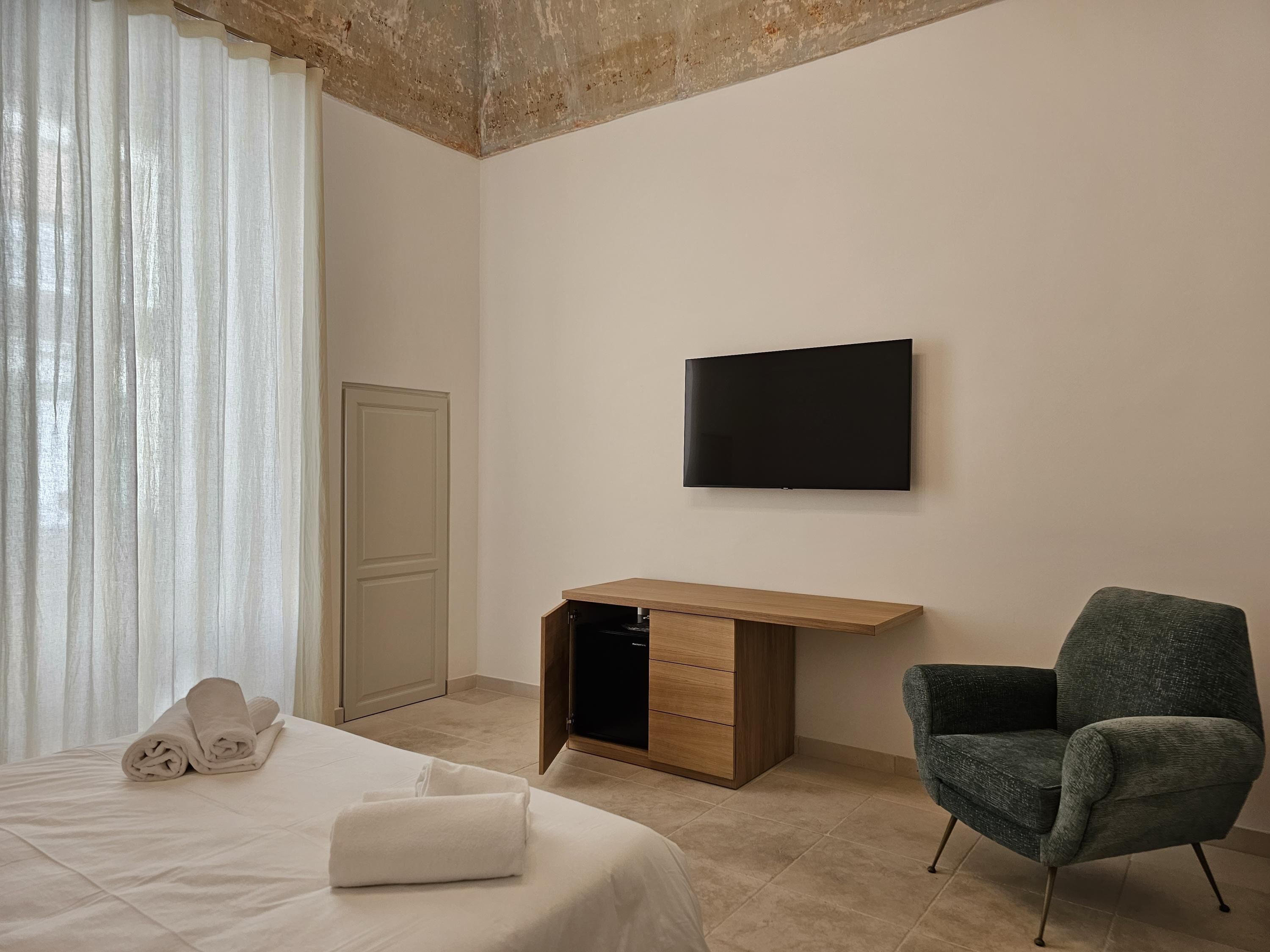 A hotel room with a bed, a desk, a chair, a TV, and a door.