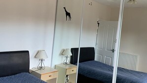 Ein Schlafzimmer mit zwei Betten, einem Spiegelkleiderschrank, einem Deckenventilator und einem Nachttisch mit Lampe.