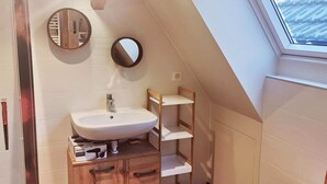 Een kleine, moderne badkamer met een houten wastafelmeubel, een witte wastafel en een toilet. Boven het toilet is een dakraam, en aan de muur hangt een spiegel.