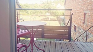 Een houten terras met een ronde tafel en rode stoelen, met uitzicht op een gebouw van baksteen en een gazon.