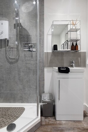 A modern bathroom with a glass-enclosed shower, a white sink with a makeup towel, and a mirror above the sink.