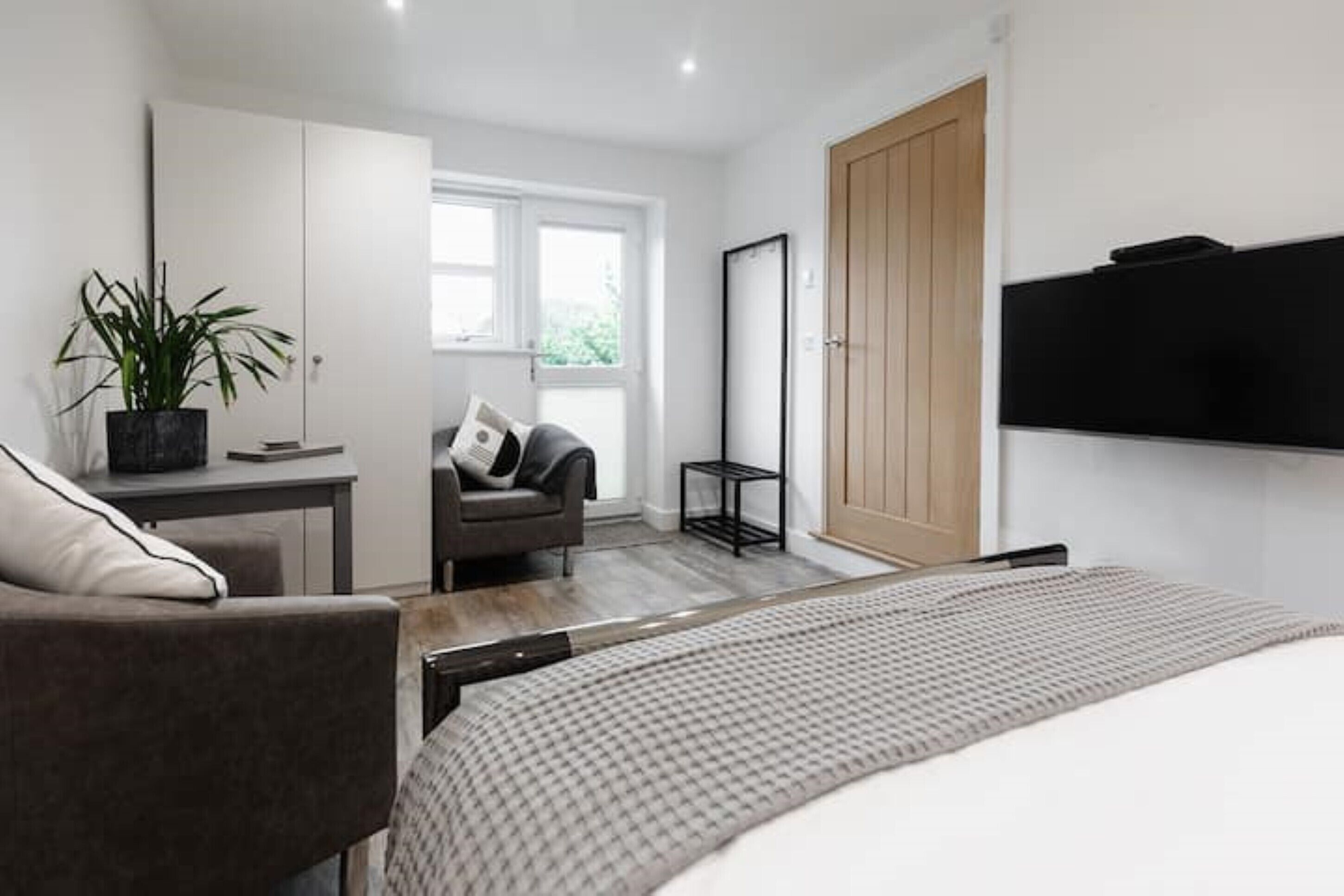Ein modernes Schlafzimmer mit Bett, Schreibtisch, Stuhl, einer Topfpflanze und einem Kleiderschrank.
