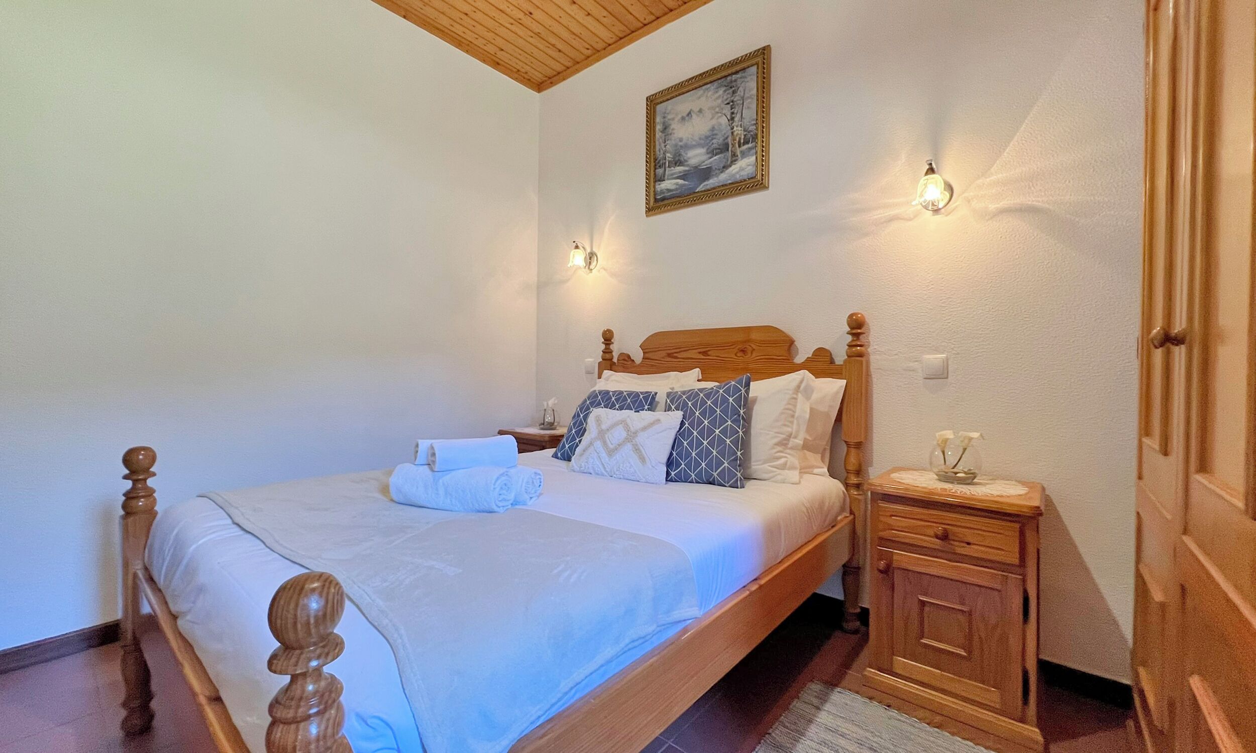 A neatly made bed with a wooden headboard, two bedside tables with lamps, and a painting on the wall.