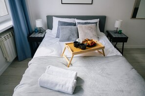 A neatly made bed with a tray of croissants and coffee, a white towel, and a view of a window with blue curtains.