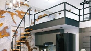 A modern living room with a blue sofa, yellow cushions, a kitchen area, and a staircase leading to an upper level. - Łódź City Center Studio - Entresol & Balcony - by Rentujemy (Lódz)