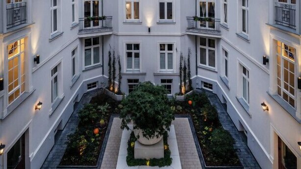 A multi-story building with balconies, a central courtyard with plants, and exterior lighting. - Łódź City Center Studio - Entresol & Balcony - by Rentujemy (Lódz)