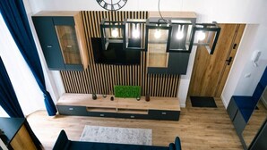 A modern living room with a built-in TV, wooden panel wall, and a blue sofa with yellow cushions. - Łódź City Center Studio - Entresol & Balcony - by Rentujemy (Lódz)