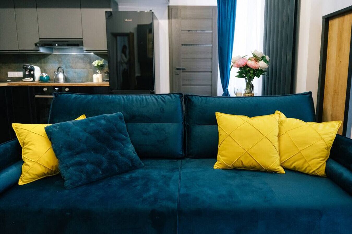 Un salon moderne avec un canapé bleu foncé, deux coussins jaunes et un vase rempli de fleurs posé sur une table en bois.
