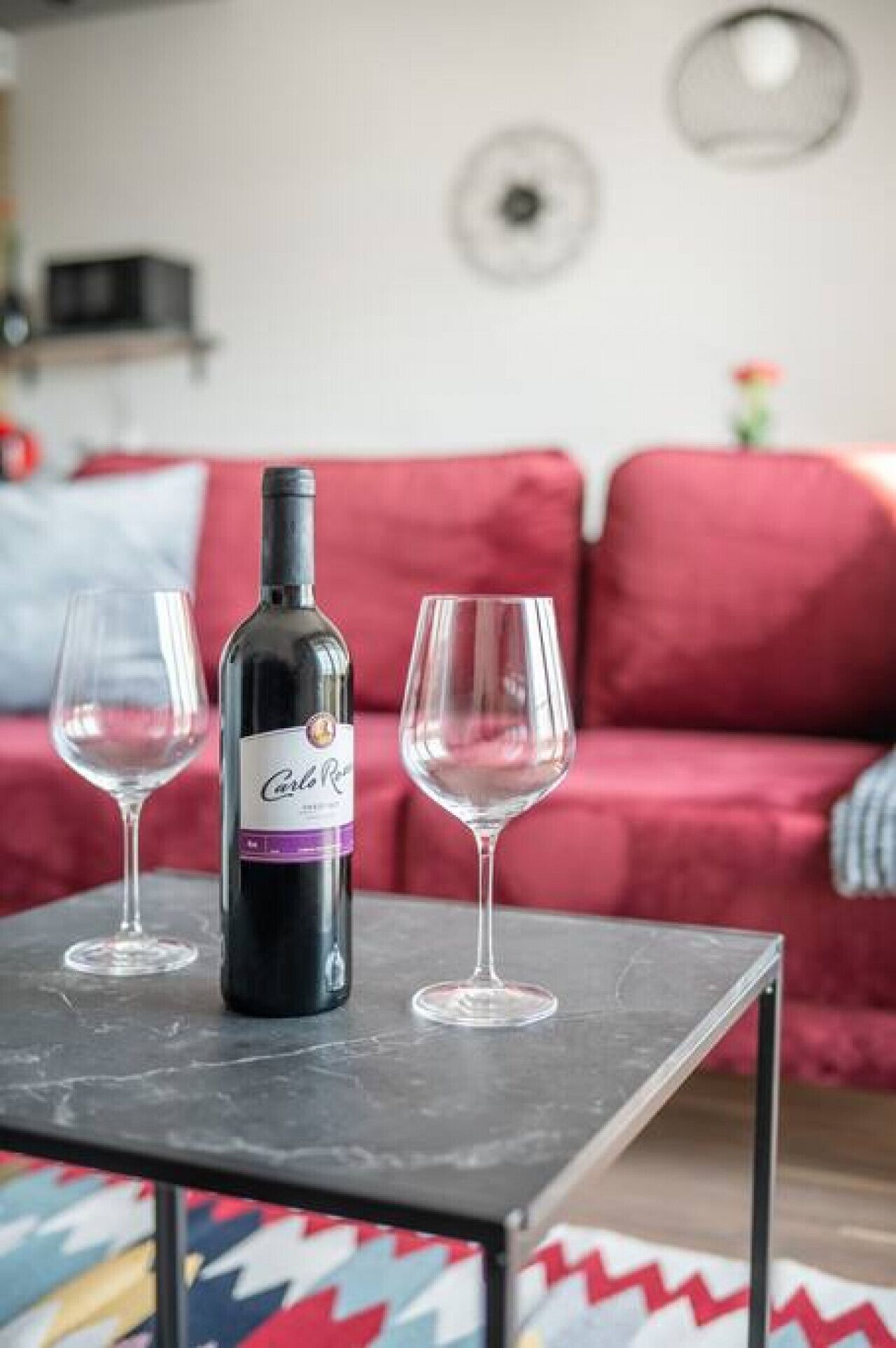 Una botella de vino y dos copas sobre una mesa en un salón con un sofá rojo.
