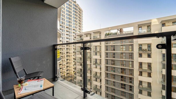 A balcony with a table, chairs, and a glass railing overlooking a high-rise building.