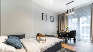 A modern bedroom with a bed, bedside table, and a dining area with chairs and a table.