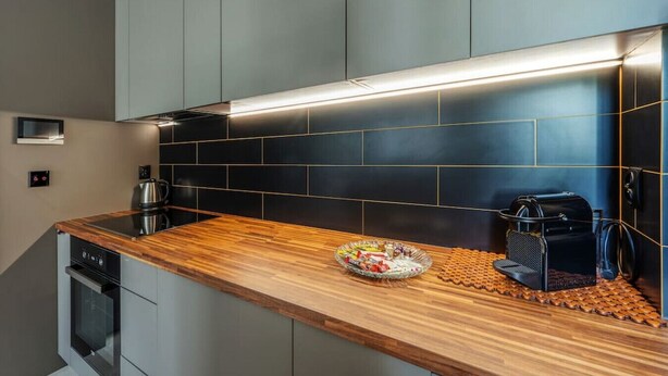 A modern kitchen with a wooden countertop, black tiled backsplash, and stainless steel appliances.