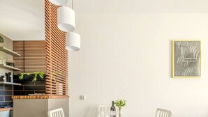 A modern dining area with a white table set for four, two white chairs, and a grey sofa in the background.