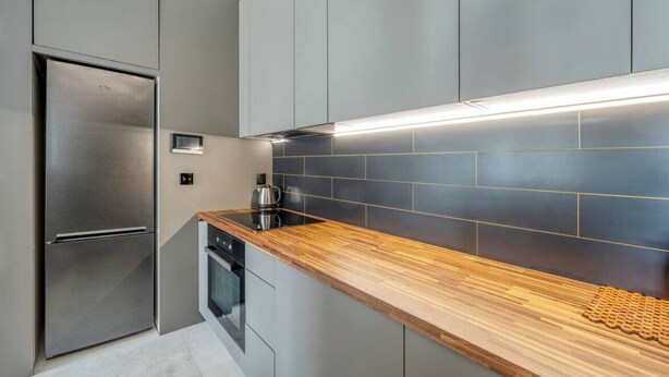 Uma cozinha moderna com geladeira de aço inoxidável, bancada de madeira e backsplash em azulejos azul escuro.