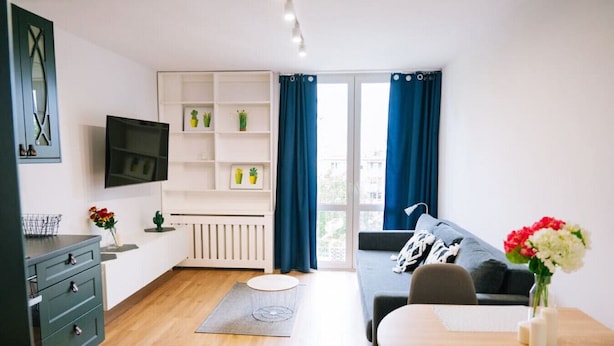 A modern living room with a sofa, a dining table, a TV, and a built-in shelf with plants. - Warsaw Studio Apartment - City View, Parks nearby by Rentujemy (Warszawa)