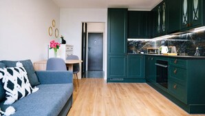 A modern living room with a sofa and a dining table, a kitchen with teal cabinets and a marble backsplash, and a door leading to another room. - Warsaw Studio Apartment - City View, Parks nearby by Rentujemy (Warszawa)