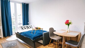 A bedroom with a bed, a desk, two chairs, a small table with a tray, and a vase with flowers. - Warsaw Studio Apartment - City View, Parks nearby by Rentujemy (Warszawa)