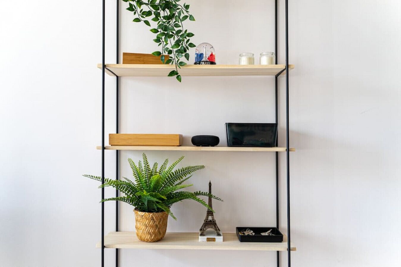 A multi-tiered wooden shelf unit with various decorative items including a small Eiffel Tower model, a potted fern, and a glass jar.
