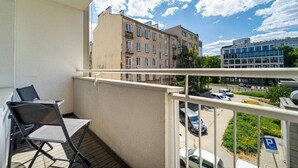 Un balcone con tavolo e sedie, affacciato su un'area di parcheggio e degli edifici.