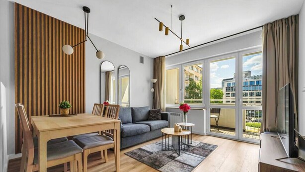 Un soggiorno moderno con tavolo da pranzo in legno, divano grigio e un balcone con vista sulla città.
