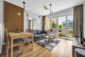 A modern living room with a wooden dining table, grey sofa, and a balcony with a city view. - Powiśle Business Apartments - Balcony, Workspace - by Rentujemy (Warszawa)