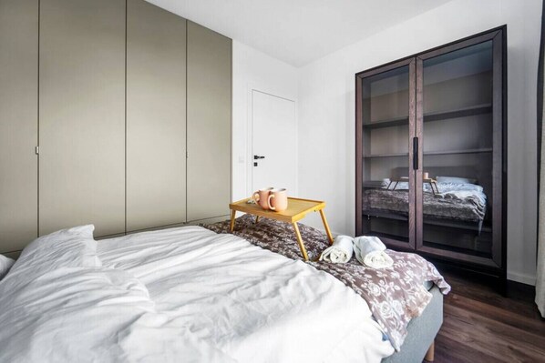 A bedroom with a bed, a wooden bedside table with a mug, a wardrobe, and a large sliding door closet.