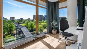 Un espacio de oficina moderno con ventanas amplias, una silla de oficina negra, un escritorio blanco y una planta en maceta.