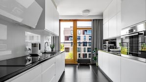 Una cocina moderna con muebles blancos, encimera negra y vista a un edificio por una puerta de cristal.