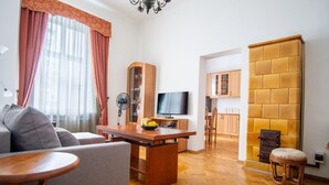 Ein modernes Wohnzimmer mit Sofa, Esstisch und Fernseher. Es gibt eine Küchenzeile mit Schränken und einer Holzwand.
