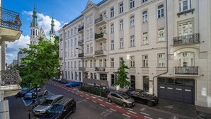 Straßenansicht einer Reihe klassischer europäischer Gebäude mit parkenden Autos und blauem Himmel.